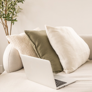 Cozy neutral living room with laptop, textured pillows, and soft minimalist decor.