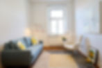 Praxis von Helgard, Heinrichs, Heller Raum mit blauem Sofa, Sessel und Fenster.
