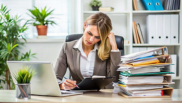 woman-sits-desk-with-laptop-stack-papers.jpg