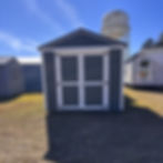 Front view of the shed showing double doors, white trim, and Hunter Green siding against a blue sky with a water tower.
