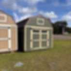 Front view, close-up. Green shed with beige doors, transom windows, and brown metal roof.