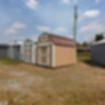 Exterior view of the brown lofted barn shed with white trim and coco brown metal roof in a grassy lot.