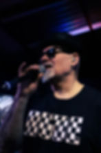 Man in sunglasses and 'RUDE' shirt singing into a microphone
