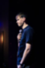 Man with microphone on stage, looking thoughtful