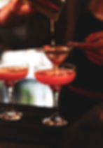 Bartender straining a red cocktail into two coupe glasses