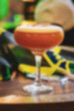 Foamy orange cocktail in a coupe glass with Jamaican flags