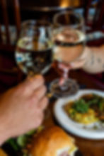 Two people toasting white wine glasses over food