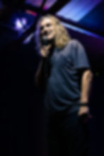Man with long hair holding a microphone on stage, smiling