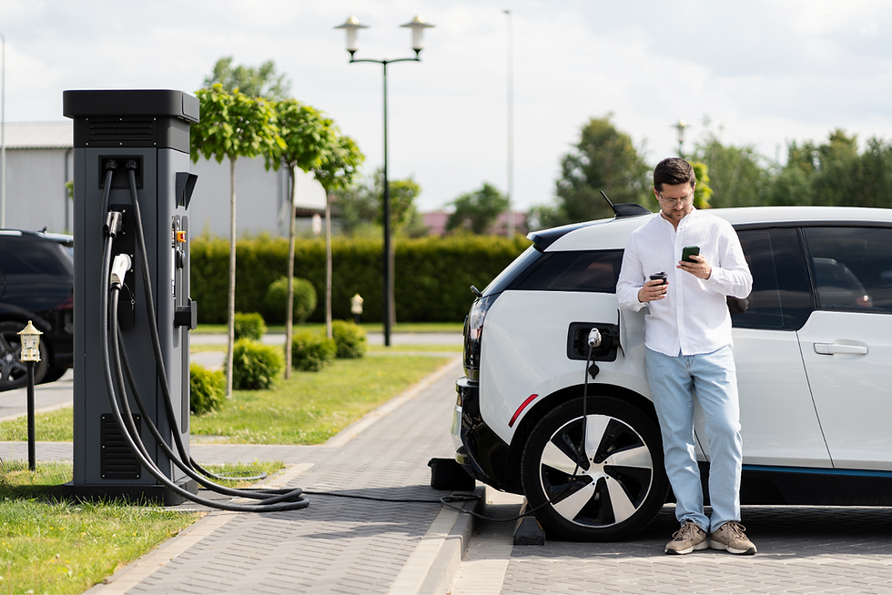 A middle-aged man stood next to his BMW electric car while it is charging at a UK public electric charging station.