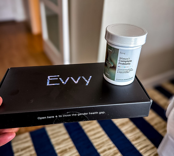 Black Evvy box with a Women's Complete Probiotic jar on top, on a striped carpet; text reads Open here to close the gender health gap.

