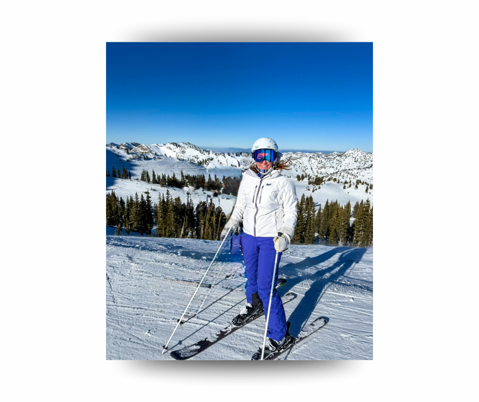 A person in a white helmet and jacket skis on a snowy mountain with evergreen trees. Clear blue sky in the background, sunny day.