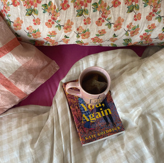stock photo of cup of tea and book sitting on checkered and flower bedding