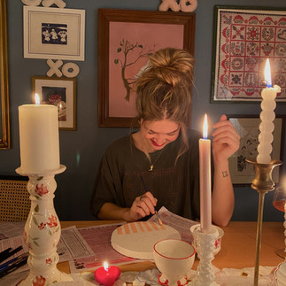 stock photo of a girl with a messy bun painting surrounded by candle light