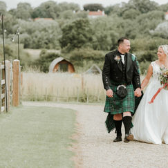 Bride and groom in kilt walking up country path holding hands
