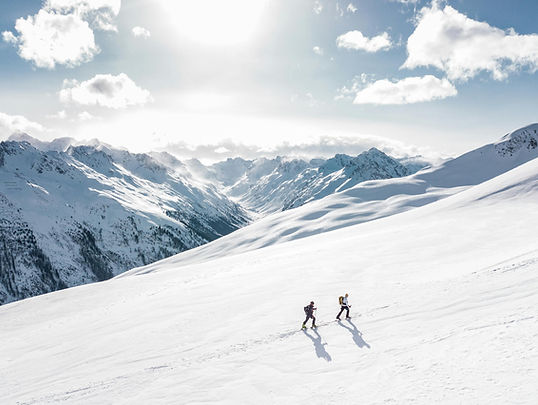 Two people hiking up a snowy mountain with a range of mountains showing in the landscape. Loyalty Program