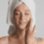 Relaxed woman with towel on head touching face at spa