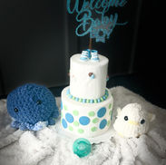 Fondant covered cake with Welcome Baby text and blue decorations on a blanket.