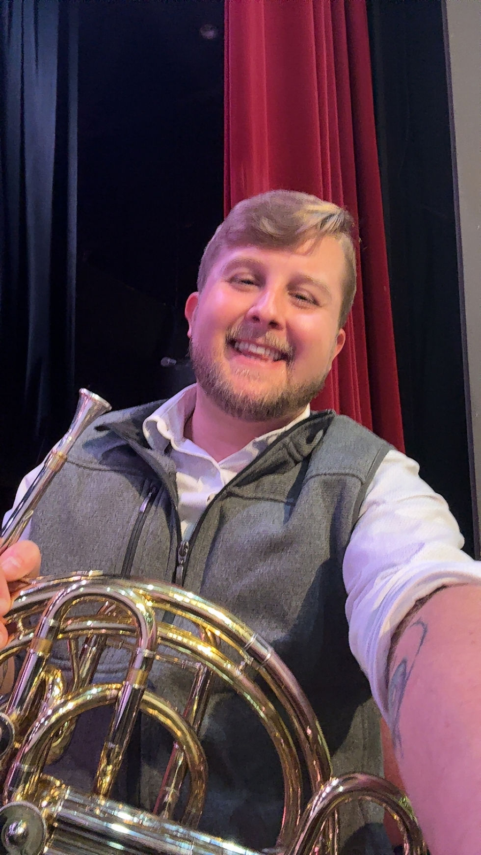 young man in a vest holding a french horn