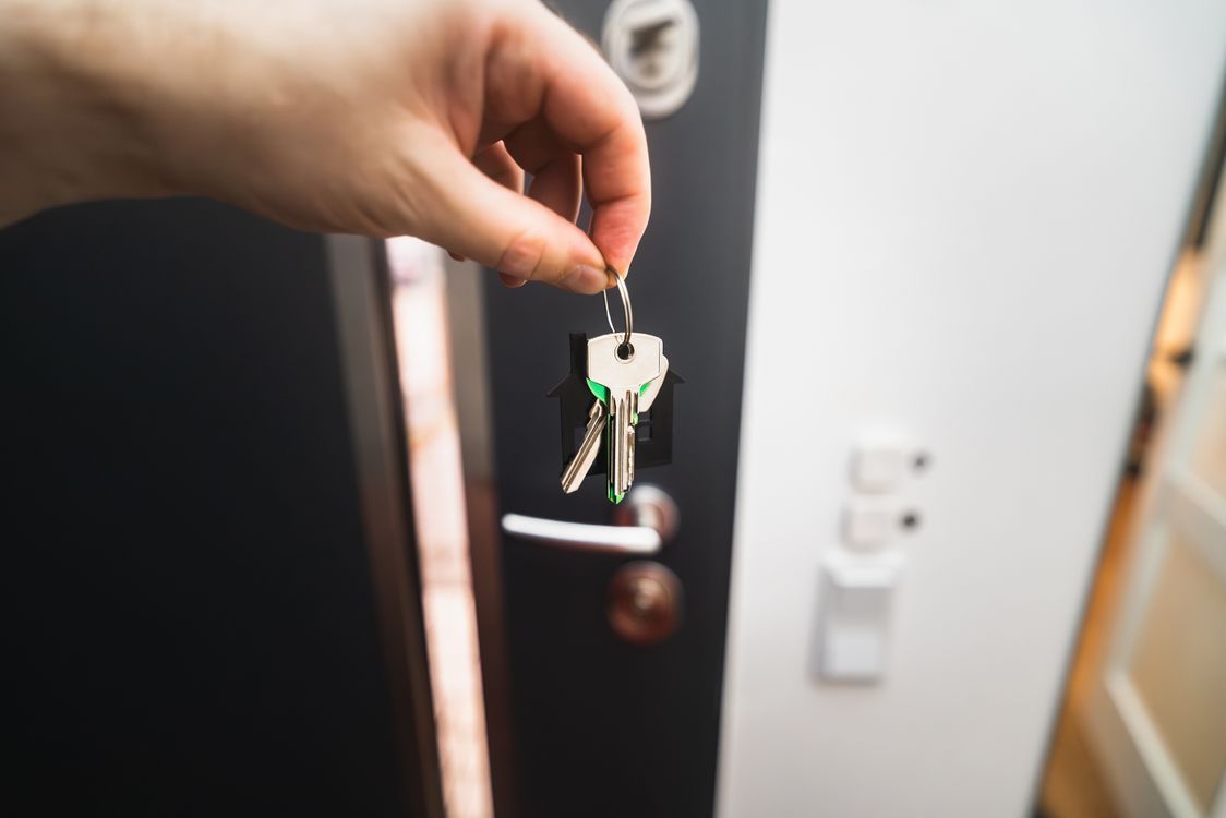 House keys with a home-shaped keyring held in front of a front door — the settlement moment BK Home Broker works toward for every buyer, at zero upfront cost