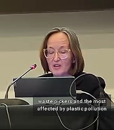 Video frame showing Barbra “Barbie” Weber seated at a long table indoors and speaking into a microphone with a laptop in front of her. She is wearing glasses and a black suit jacket. Behind her is a plain gray wall. The caption from this part of her INC-4 speech showing up in the frame reads, "waste pickers and the most affected by plastic pollution"