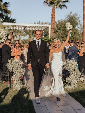 Bride and groom walk down the aisle while the guests look on. Bride raises her bouquet.