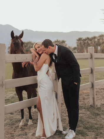 Groom kisses brides shoulder while they pose with a horse