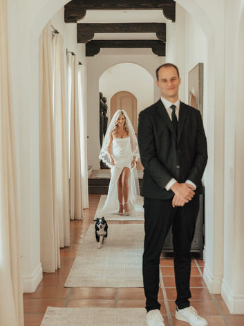 Bride and her dog walk up behind groom in a long hallway at the emerson estate