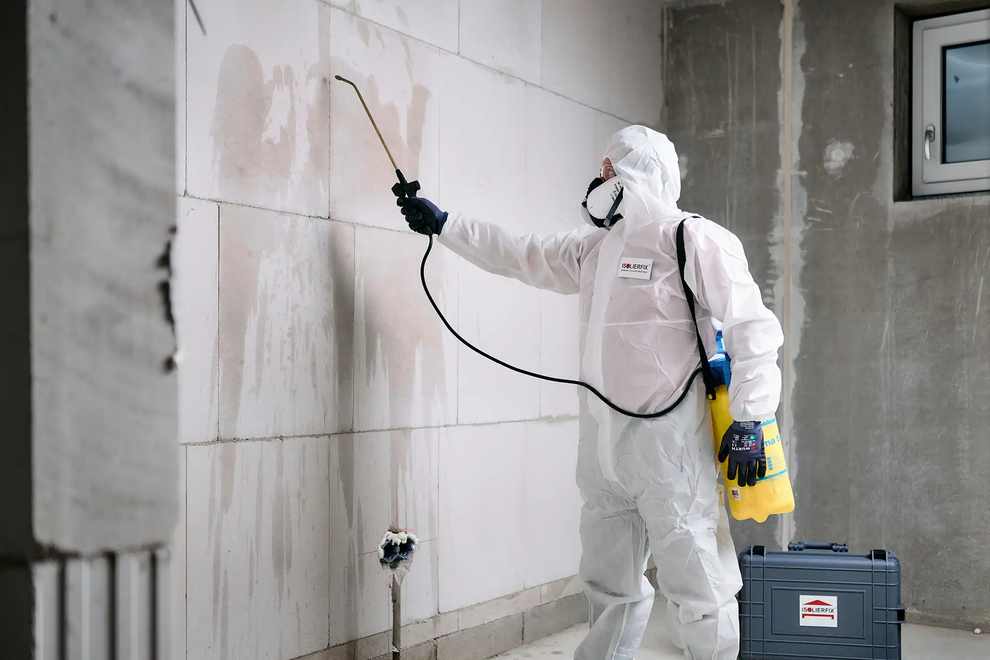 ISOLIERFIX-Mitarbeiter im weißen Schutzanzug bei der Schimmelbeseitigung mit Sprühgerät – dokumentiert für eine Fotoreportage im Bereich Bau- und Sanierungshandwerk