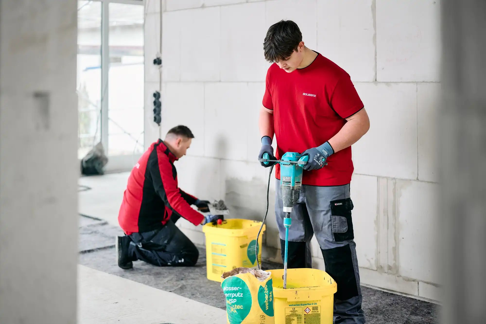 Zwei Mitarbeiter von ISOLIERFIX bereiten auf einer Baustelle Baustoffe vor, fotografiert für eine inszenierte Handwerksdokumentation