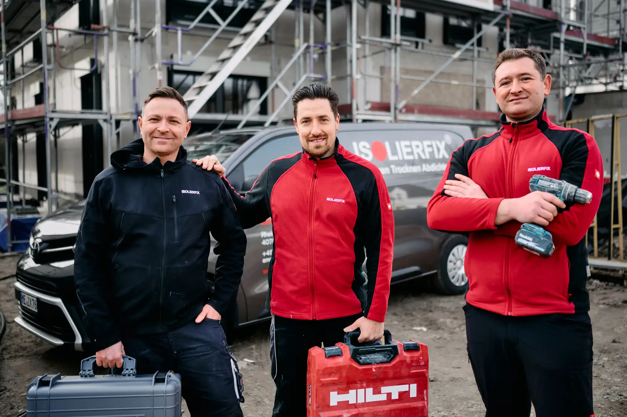 Drei Handwerker der Firma ISOLIERFIX stehen mit Werkzeugkoffern vor einer Baustelle, fotografiert für eine Unternehmensreportage im Bereich Handwerksfotografie