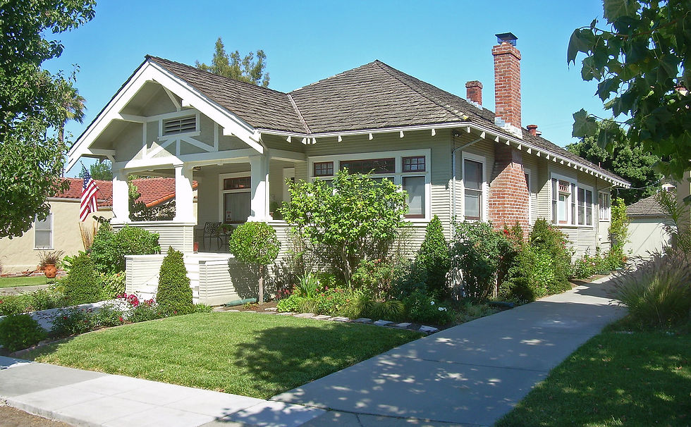 Bay area home with a brick chimney, lush garden, and an American flag in a sunny suburban setting in a Bay Area neighborhood in California. White trim contrasts with soft green siding.