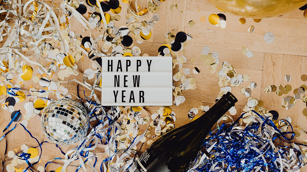 Confetti and ribbons scattered around a "Happy New Year" sign, disco ball, and champagne bottle on a wooden floor, creating a festive mood.
