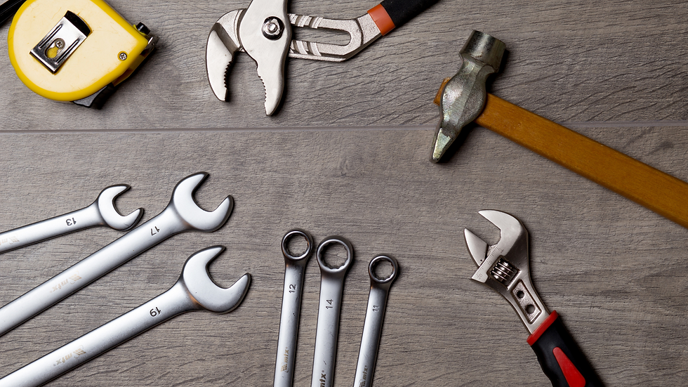 Assorted tools on a wooden surface: yellow tape measure, pliers, wrench, and hammer. Silver wrenches labeled with numbers.