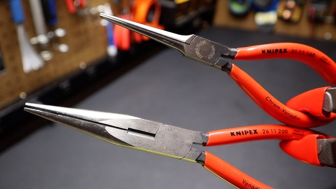 Red-handled pliers with long, pointed noses are held in focus against a blurred workshop background. Visible text: Knipex.