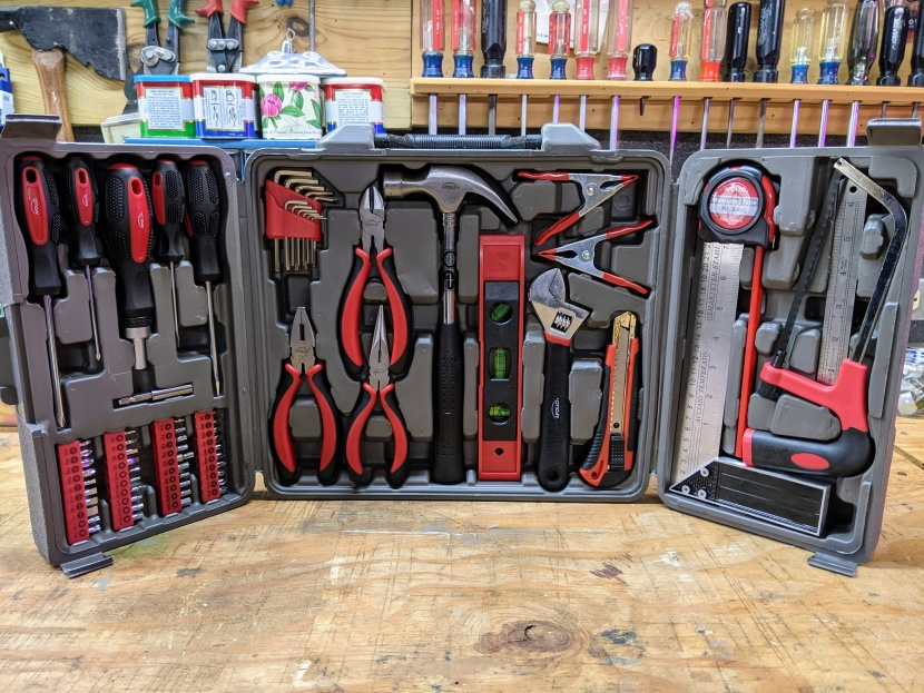 Open tool case with assorted tools in a workshop. Tools include pliers, a hammer, and screwdrivers. Red and black color theme.