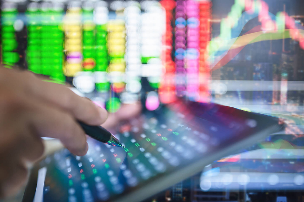 Hand using a stylus on a tablet displaying financial data. Colorful stock charts and numbers fill a blurred screen background.