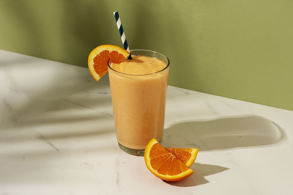 Orange smoothie with a striped straw, garnished with orange slices, on a white marble surface against a green background. Bright and refreshing.