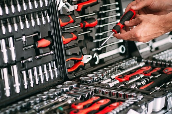 Hands sorting a black and red tool kit with wrenches, screwdrivers, and sockets. The setting is bright and organized.