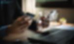 Person holding a credit card and phone near a laptop, with virtual shopping icons. Dimly lit office setting, creating a focused mood.
