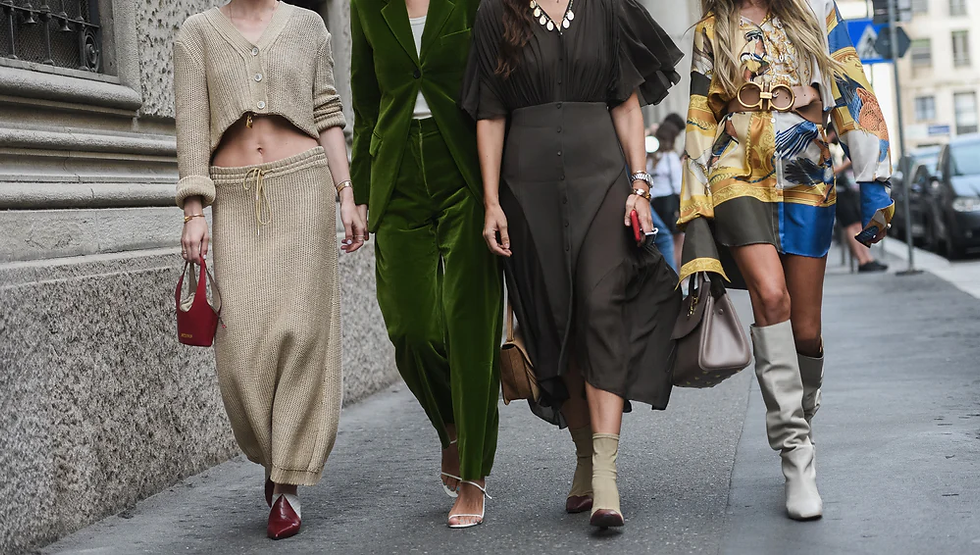Four fashionable women walking on a city street, each wearing distinct stylish outfits in neutral and vibrant colors, exuding confidence.