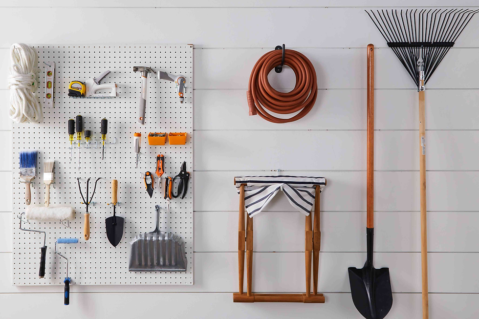Tools neatly organized on a white pegboard, including hammers, screwdrivers, ropes, and garden tools. A coiled hose and rake are mounted nearby.