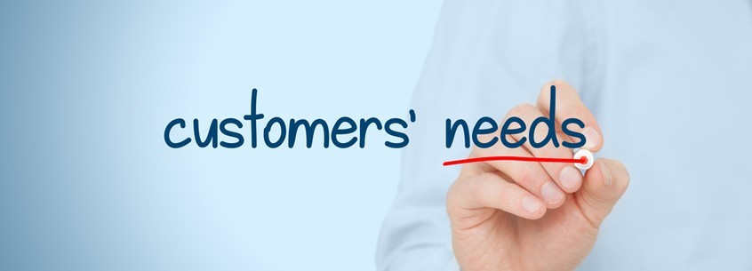 Hand writing "customers' needs" in blue with a red underline on a light blue background, conveying focus on customer priorities.