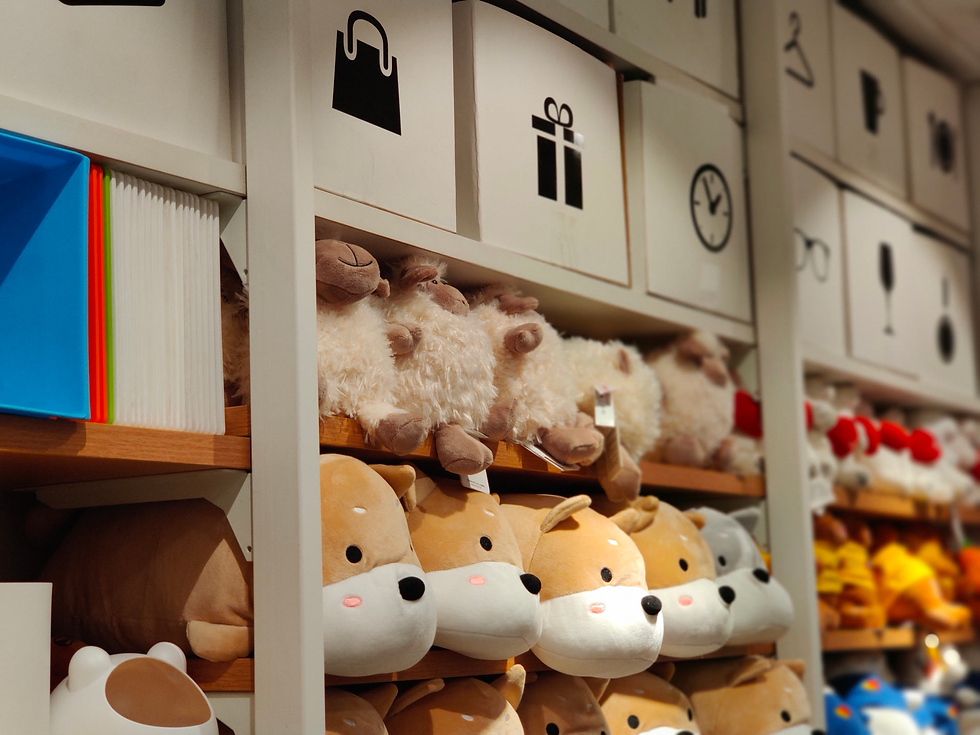 Stuffed animal toys, including sheep and dogs, are neatly stacked on shelves in a store. White boxes with symbols are on top shelves.