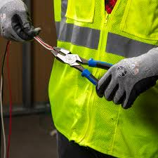 Person in a neon yellow safety vest using blue-handled pliers to cut wires. Wears gray gloves. Indoor setting with a muted background.