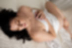Boudoir Minneapolis Metro Woman lying on a bed, draped in white fabric, eyes closed, peaceful expression. Soft lighting, white textured blanket.
