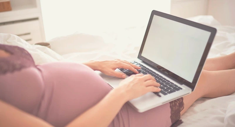 Pregnant person typing on laptop internet search for childbirth education