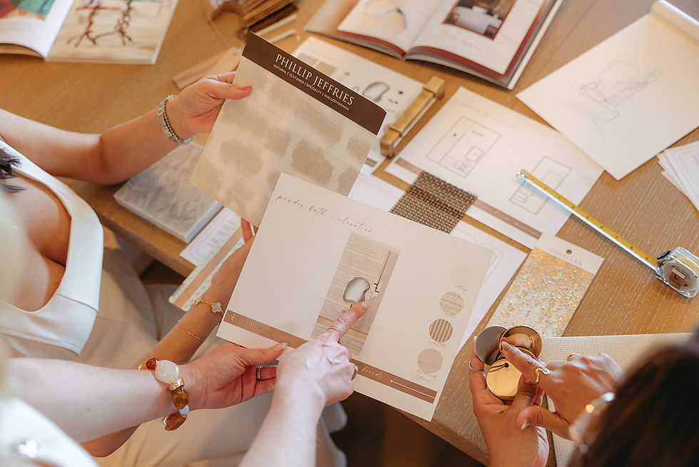 People choosing wallpaper and fabric samples at a table, with Phillip Jeffries swatch book, design boards, books, and ruler.