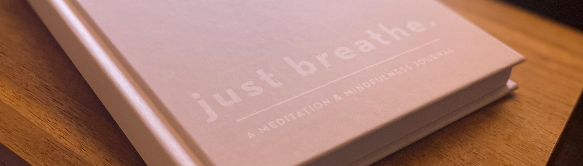 Pink journal with “just breathe” on the cover, resting on a table in the Still Bloom office.