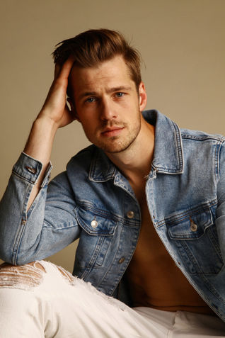 Male model Krystian Nowak in a blue denim jacket and white denim jeans.