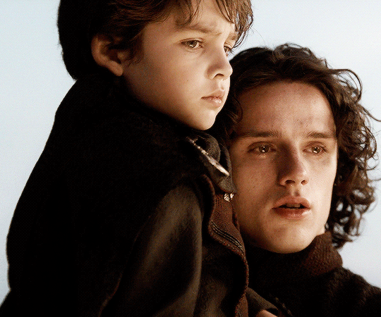 An animated GIF image of Harry Collett as Prince Jacaerys, holding his younger brother, with a mournful expression and moist eyes.